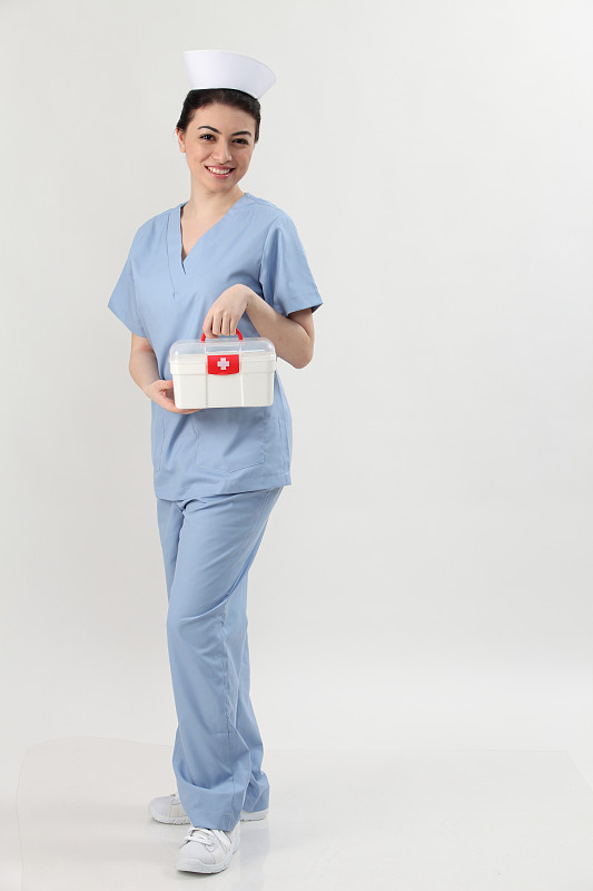 在灰色背景下，快乐的年轻女性护士抱着急救箱的全长肖像图片素材