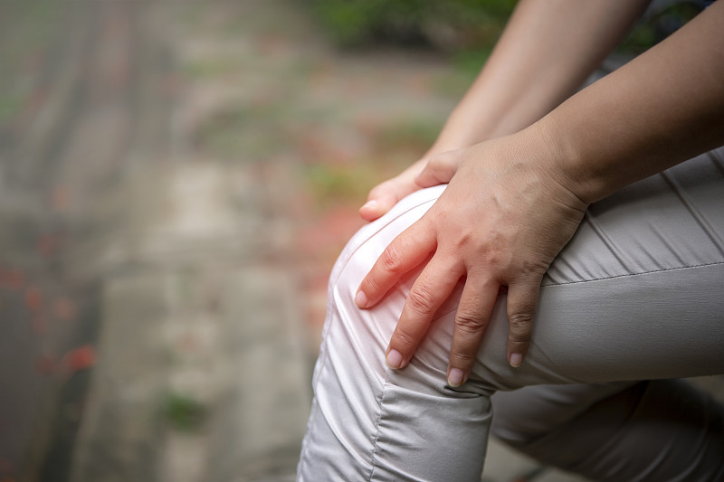 一位老妇人在公园里饱受膝盖疼痛之苦。抱着膝盖，用手按摩。图片素材
