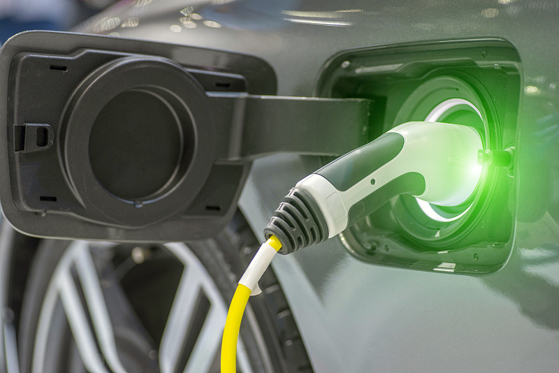 混合动力汽车电动充电站的特写与电源插入电动汽车正在充电。图片下载