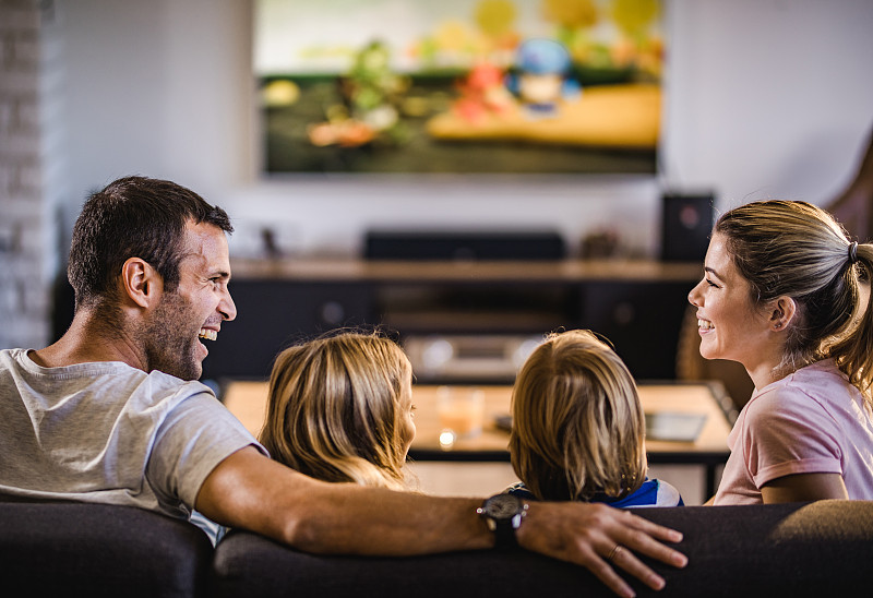 快乐的父母在家里和孩子们一起看电视的时候聊天。图片素材