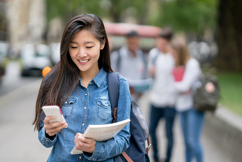 亚洲女学生在户外用手机发短信图片素材