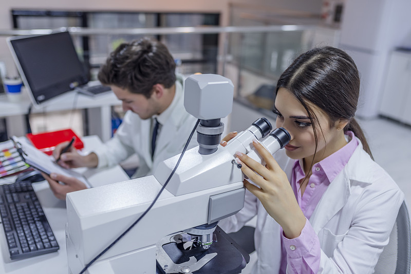 一位女科学家通过显微镜观察的侧视图图片下载