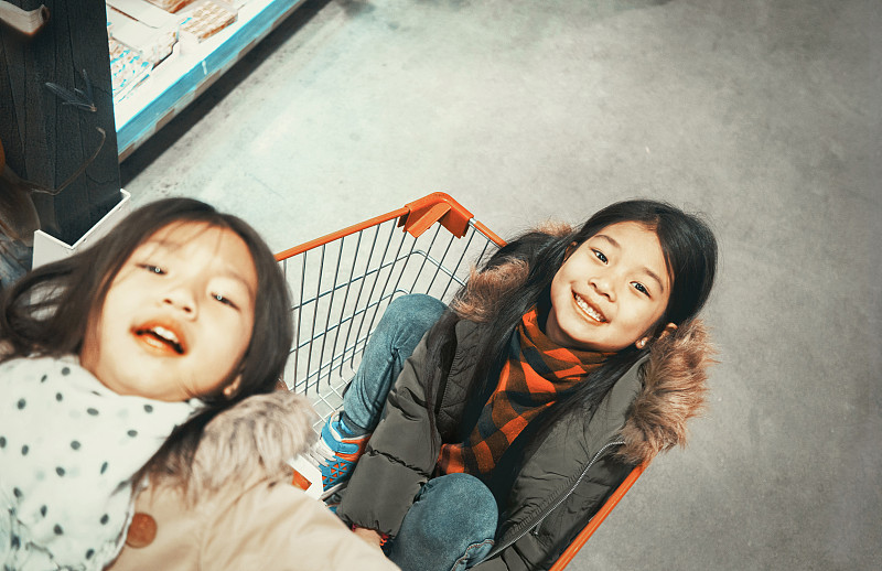 两个女孩坐在超市的购物车里图片下载