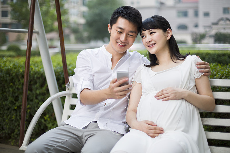 丈夫和怀孕的妻子在摇椅上听音乐图片下载
