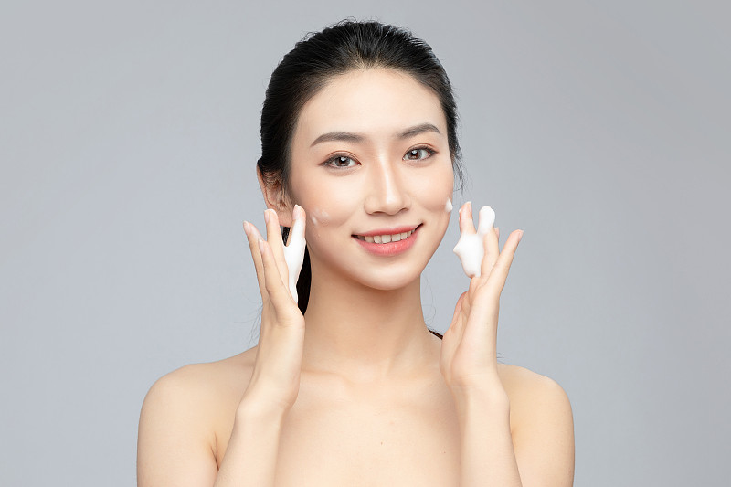 灰色背景里正在使用洗面奶的亚洲美女面部特写，化妆护肤整容图片下载