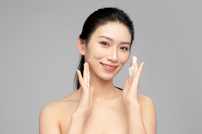 灰色背景里正在使用洗面奶的亚洲美女面部特写，化妆护肤整容图片下载
