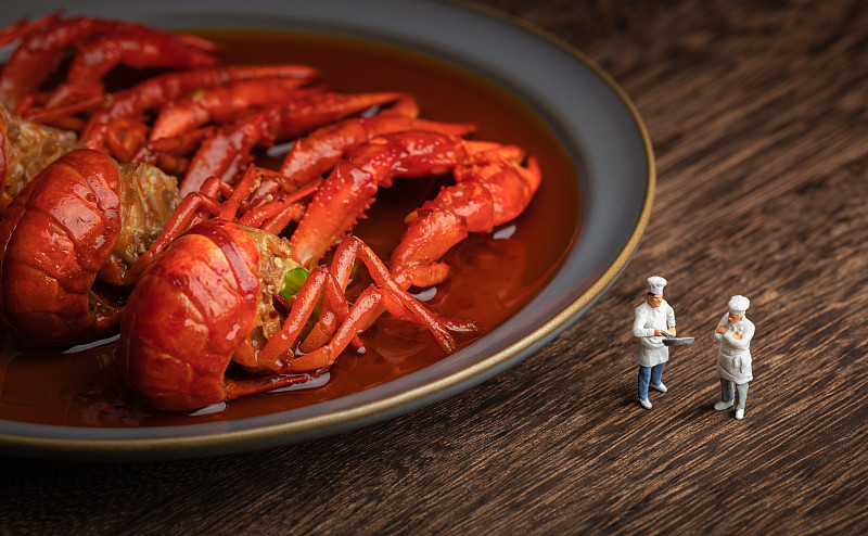 木桌上盘子里的麻辣小龙虾与厨师图片下载