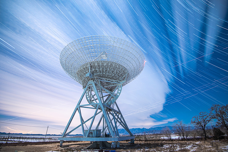 夜间射电望远镜在星空和云的流动下静静矗立在大地上图片素材