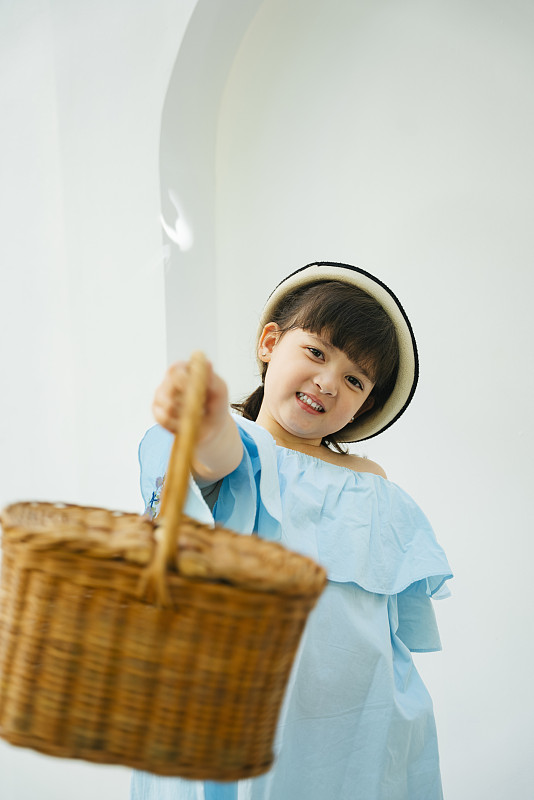 亚洲孩子的肖像，浅蓝色的裙子，手持木篮子在白色的背景。图片下载