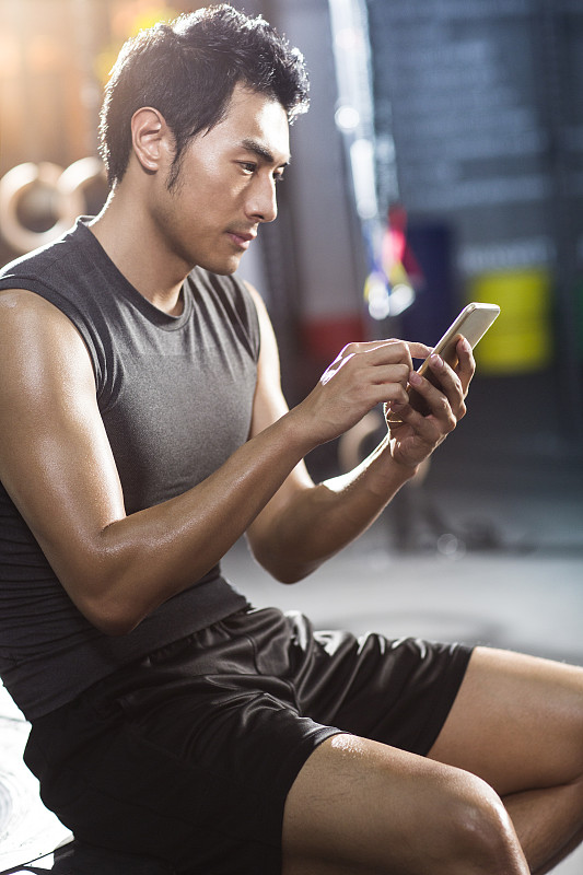 年轻男子坐在健身房使用手机图片下载