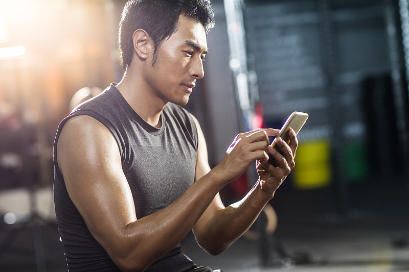 年轻男子坐在健身房使用手机图片下载