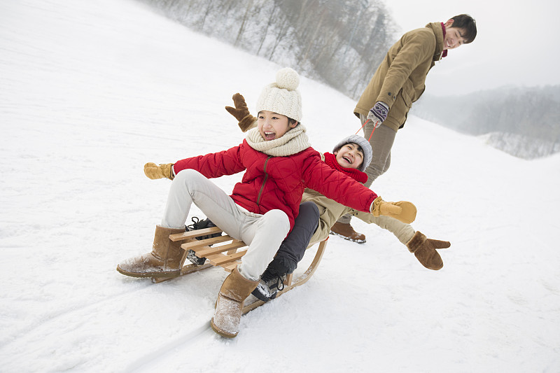 年轻的父亲和儿女在雪地上玩雪橇图片下载