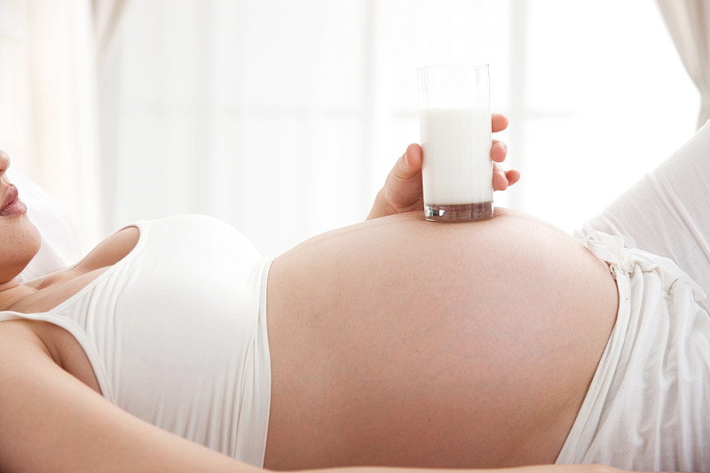 孕妇拿牛奶放在肚子上图片下载