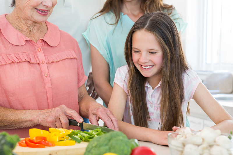 微笑的女孩看着奶奶在厨房切蔬菜图片下载