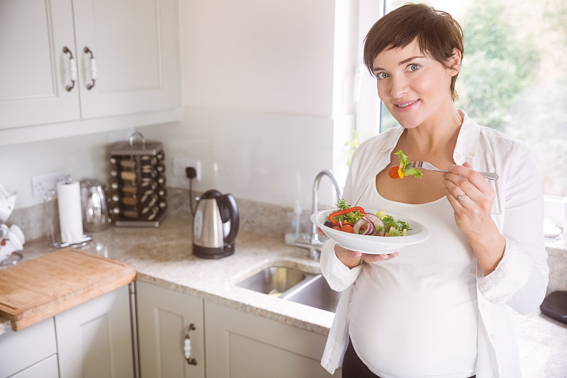 孕妇在家厨房里吃着一碗沙拉图片素材