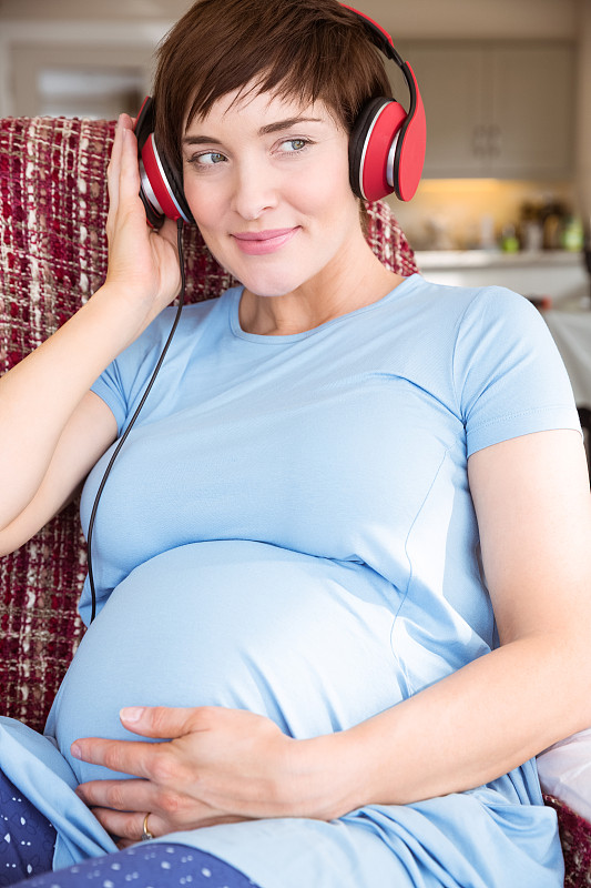 一名孕妇在起居室里戴着耳机图片下载