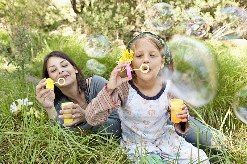 母亲和女儿(10-12)坐在草地上吹泡泡图片下载