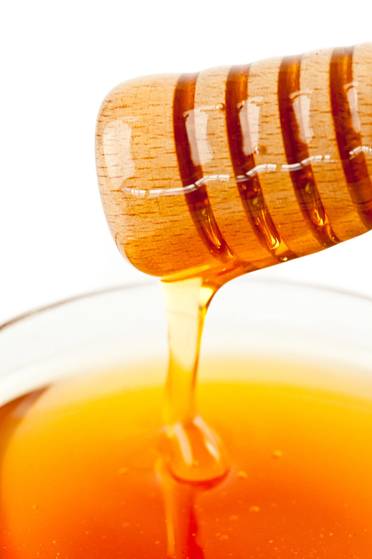 在白色的背景下，蜂蜜从勺子上滴落到蜂蜜碗里图片素材