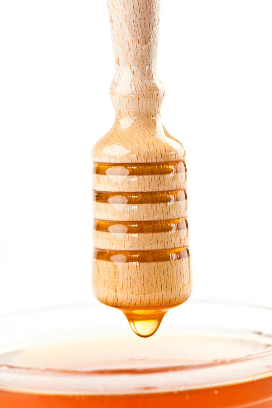 在白色的背景下，蜂蜜滴在蜂蜜碗的顶部图片下载