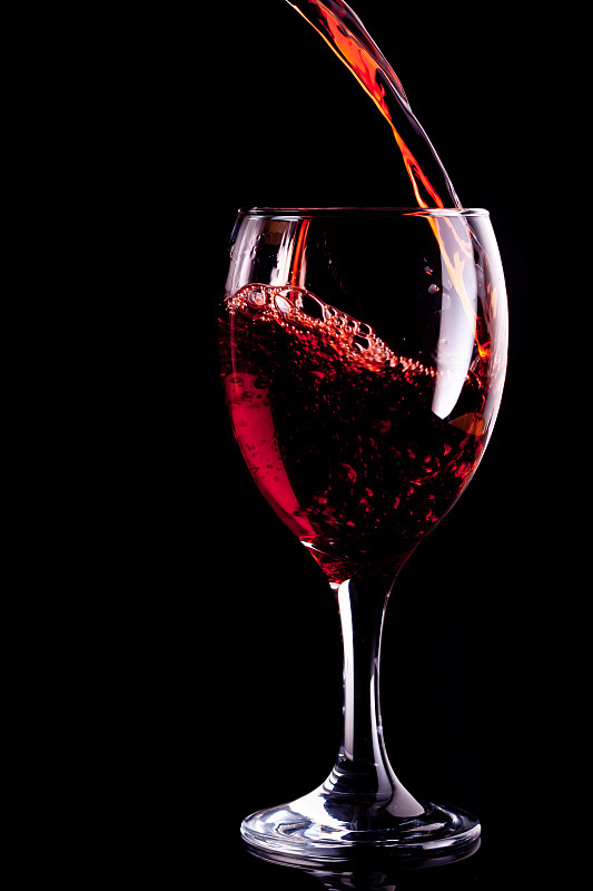 在黑色的背景下，红酒被倒入玻璃杯中图片素材