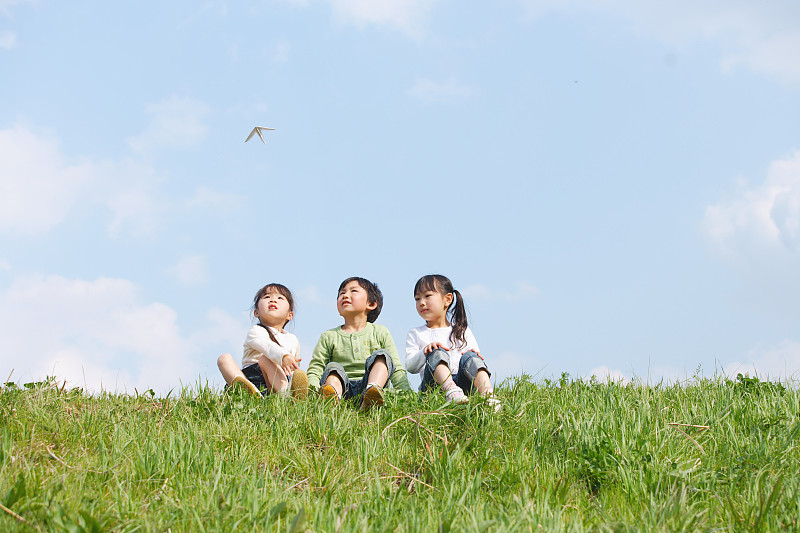 孩子们坐在公园里，看着飞翔的纸飞机图片素材