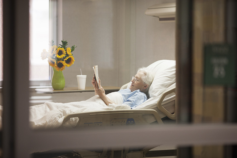 老年妇女躺在病床上看书图片下载