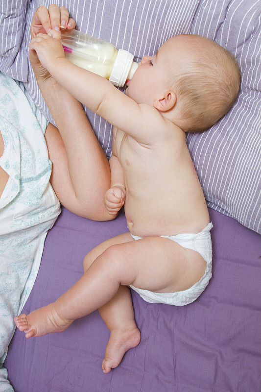 婴儿在床上喝奶瓶里的牛奶图片下载