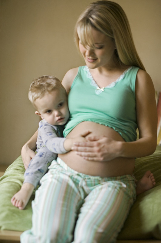 年轻孕妇抱着儿子(4-5)在床上摸肚子图片下载