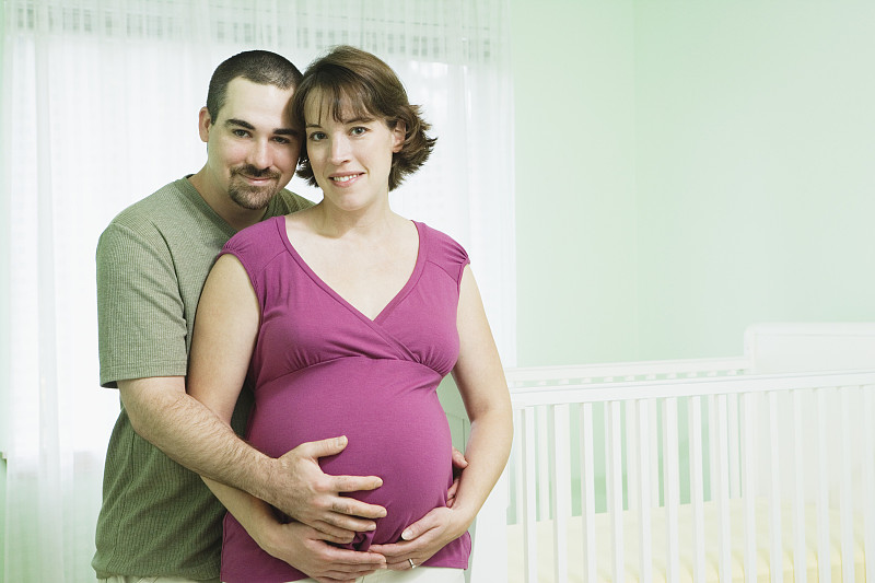男人和孕妇在婴儿室抚摸着女人的肚子，肖像图片下载
