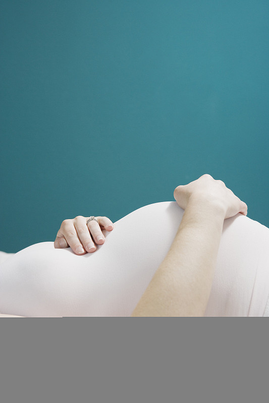 孕妇躺在床上，双手放在腹部，侧视，中段图片下载