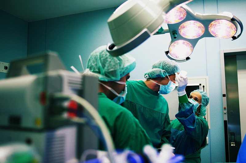 手术室团队在工作，妇女在擦拭外科医生的额头图片下载