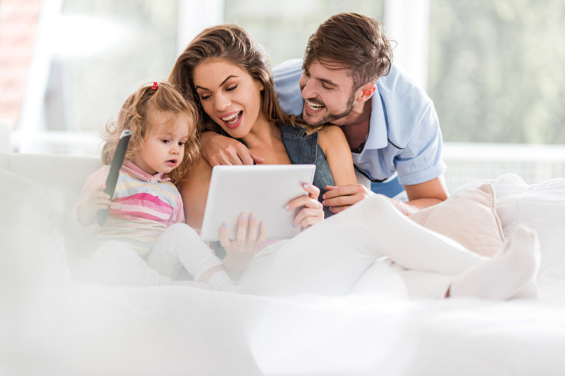 年轻快乐的父母和他们的女儿一起使用数字平板电脑。图片下载