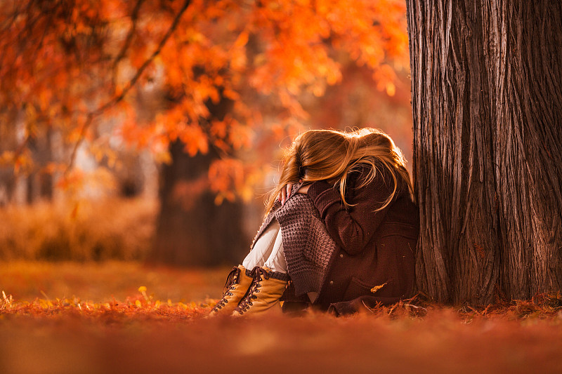 秋日里坐在公园里的伤心女人。图片下载