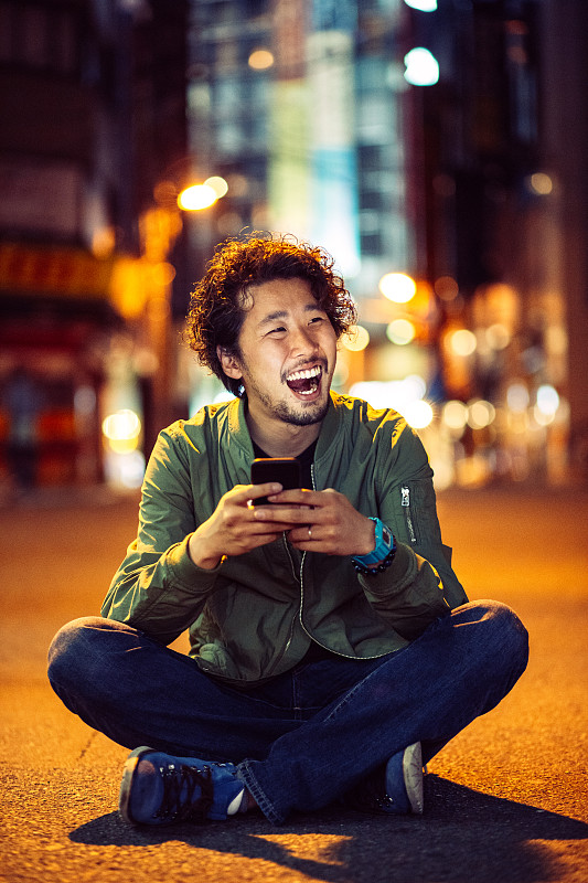 一名年轻的日本少年晚上在户外拿着手机微笑图片下载