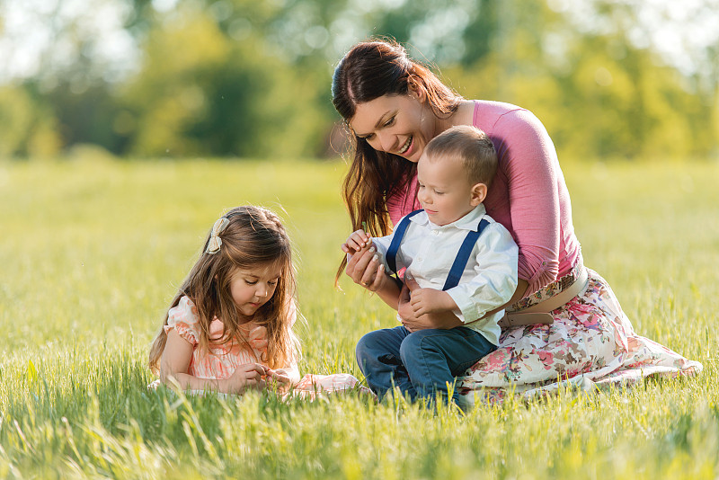 微笑的母亲和她的孩子们在草地上享受。图片下载