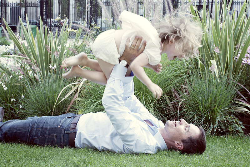 父亲躺在草地上，开玩笑地把小女儿举到空中图片下载