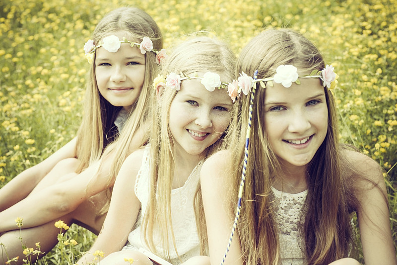 三个女孩戴着花圈坐在鲜花草地上的肖像图片下载