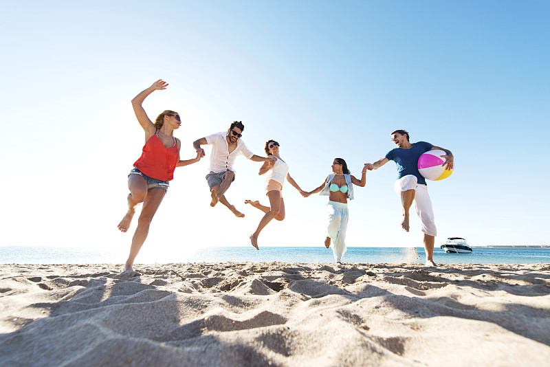 快乐的年轻人在海滩上跳跃。图片下载