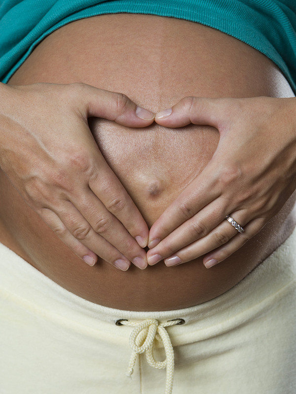 一个孕妇用她的手在她的肚子上做一个心形的特写图片下载
