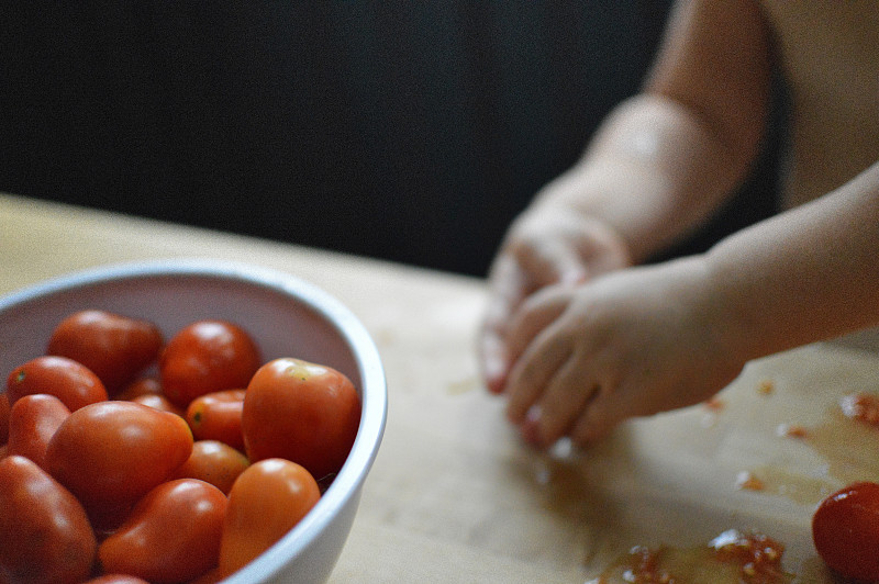 孩子在厨房削西红柿。图片下载