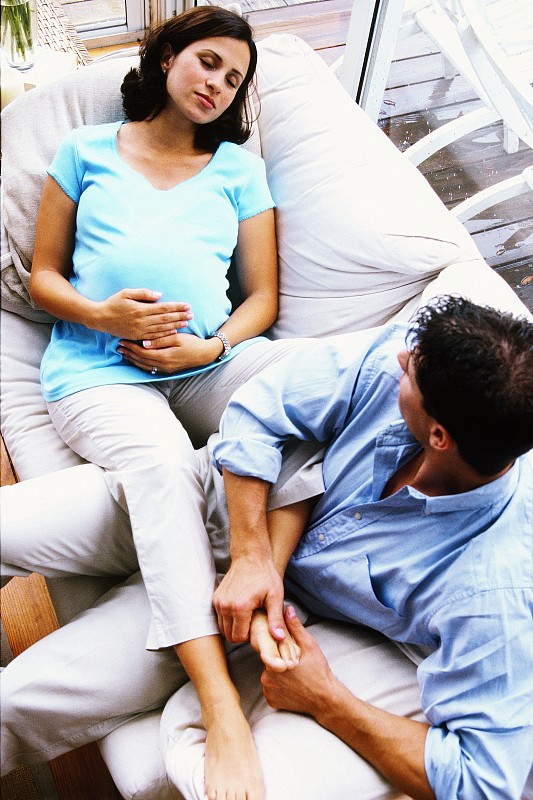 一个孕妇躺在沙发上，腿放在她丈夫的高角度视图图片下载