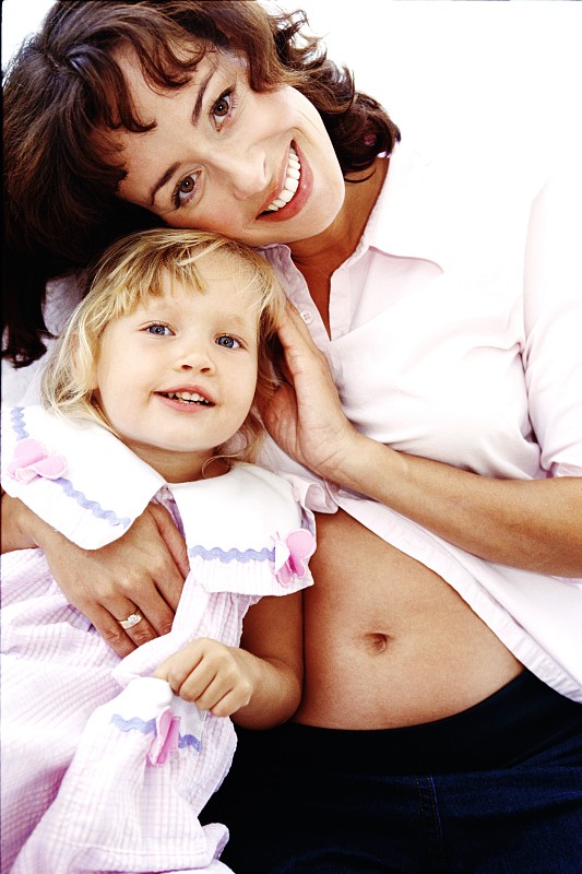 一个怀孕的母亲拥抱她的女儿和微笑的肖像图片下载