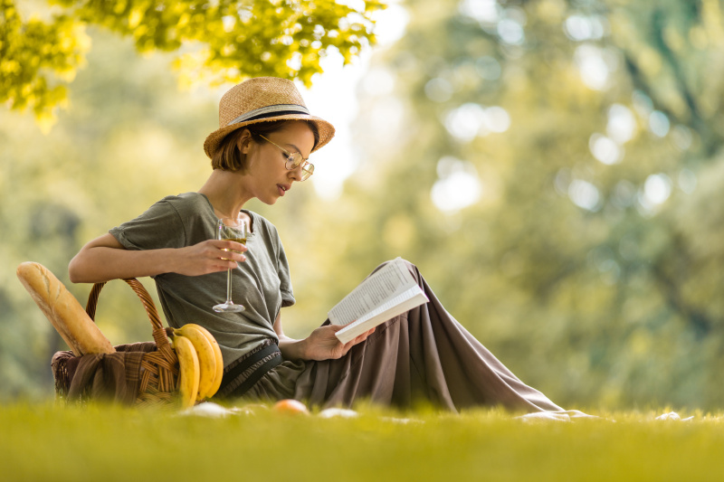 年轻女子放松与葡萄酒杯和阅读书籍在野餐。图片素材