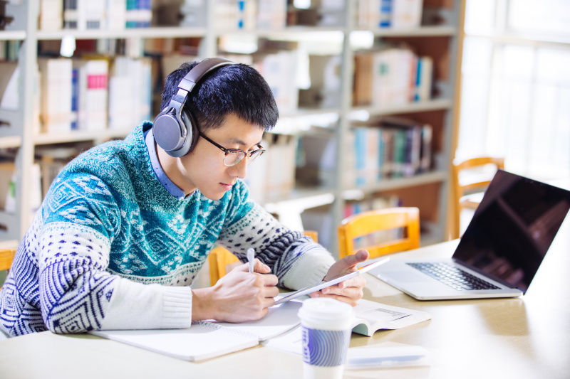 年轻的亚洲人戴着耳机在图书馆里拿着平板电脑图片下载