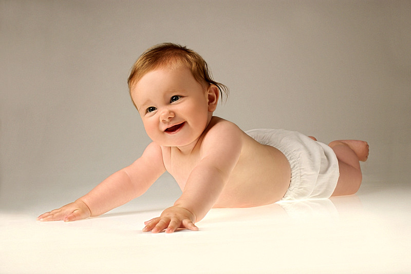 一个微笑的婴儿穿着尿布躺在她的腹部和推她的胳膊图片下载