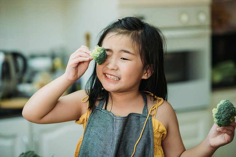 在厨房里，亚洲华人女孩手捧花椰菜，面带微笑地放在眼前，表现得很可爱图片下载