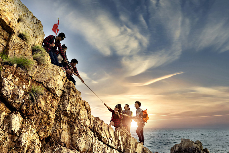 男性和女性的徒步旅行者正在攀登山崖。帮助和团队合作的理念。图片素材