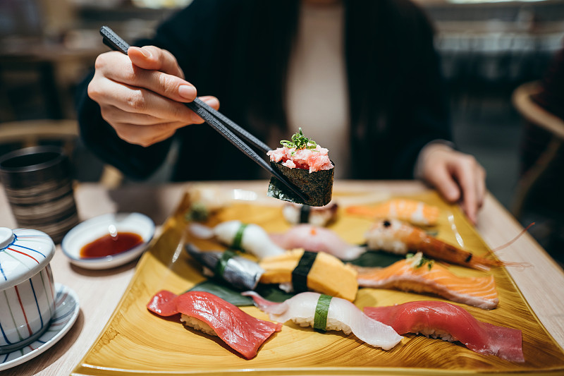 年轻的亚洲女人吃新鲜做的寿司配菜和绿茶在日本餐厅的特写图片下载