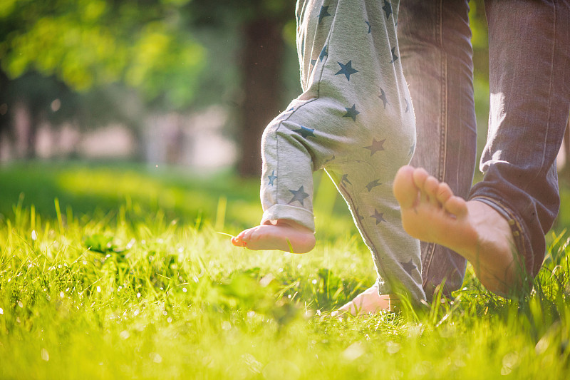 在夏天的草地上，小男孩很高兴他的父亲扶着他迈出了第一步图片素材