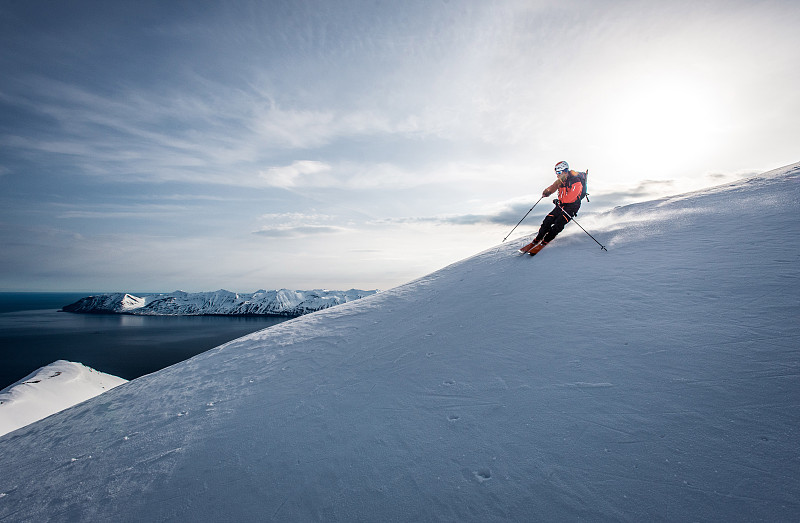 在冰岛，一名男子以海洋为背景滑雪下山图片下载